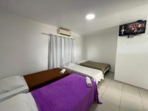 two beds in a small room with purple sheets at Pousada Anadia in Cajá