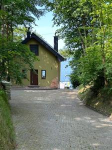 a small yellow house on a road with trees at Jarski Domek in Stężyca