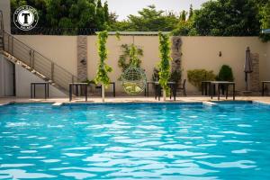 uma piscina com água azul, mesas e vinhas em Tahir Guest Palace Suites em Kano
