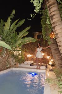 a woman in a white dress standing next to a swimming pool at Chalé da sereia apart-hotel Oásis no centro de jericoacoara in Jericoacoara