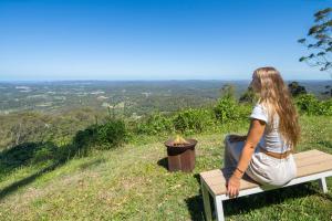 a woman sitting on a bench next to a fire pit at Montville Retreat With Hinterland & Coastal Views in Montville