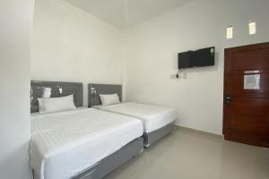 two beds in a white room with a tv at Guesthouse Pondok Amak in Padang