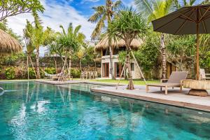 a pool with an umbrella and chairs and a house at Acacia Bungalows Bingin in Uluwatu