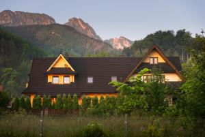 a house with a black roof with mountains in the background at Apartamenty & Pokoje MyWy in Zakopane
