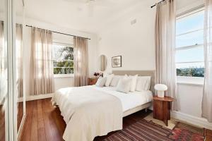 a white bedroom with a bed and a window at Coogee Treetops in Sydney