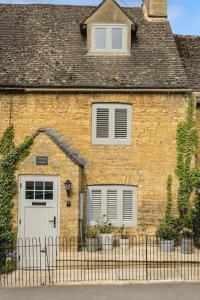 ein Backsteinhaus mit einer weißen Tür und einem Zaun in der Unterkunft Bourton-on-the-Water Lovely 2Bed Cotswold Cottage in Bourton on the Water