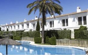 a building with a palm tree and a swimming pool at El Rompido - Punta Coral in El Rompido