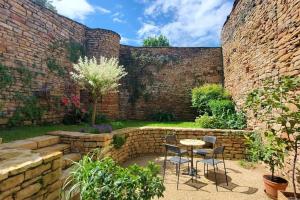 a patio with a table and chairs in front of a brick wall at Maison romane avec jardin dans le centre de CLUNY in Cluny