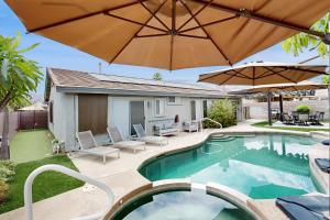 a swimming pool with an umbrella and chairs and a patio at Deerbrook Manor Permit# 67085 in La Quinta