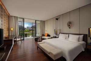 a bedroom with a large white bed and a living room at Radisson Blu Bali Uluwatu in Uluwatu