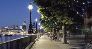 a sidewalk with people sitting on benches next to a river at Great location room in central London - Waterloo in London +2 photos