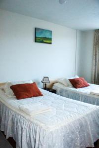 a bedroom with two beds with white sheets and red pillows at Apartamento Colca 's Home, cuenta con dos habitaciones in Chivay