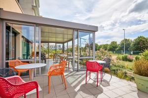 a patio with red chairs and tables and windows at Hôtel Goodwood Caen Mémorial in Caen