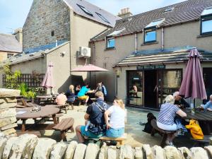 un grupo de personas sentadas en mesas fuera de un edificio en St Margaret's Hope Backpackers Hostel, en Islas Orcadas 5 fotos más