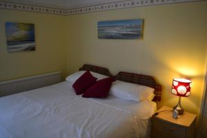 a bedroom with a white bed with red pillows and a lamp at Knightsrest in Burnham on Sea