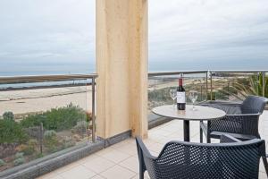a table with two glasses of wine on a balcony with the beach at Beachfront Serenity Glenelg in Glenelg