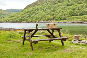a picnic table with a bottle of wine and a basket at Sawmill Cottage in Acharacle