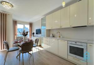 グダニスクにあるLaura Apartment with Sauna & Gym, 5 Min to Baltic Sea & Polsat Plus Arenaの白いキャビネットとテーブルと椅子のあるキッチン