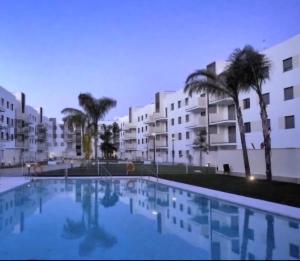 a large swimming pool with palm trees and buildings at Green Simon - Piso nuevo con Piscina 2024 in San Juan de Aznalfarache