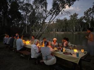 un grupo de personas sentadas en una mesa junto a un lago en Murray Life Adventures, en Torrumbarry