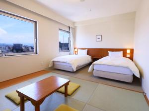 a bedroom with two beds and a table and a window at Dormy Inn Kanazawa Natural Hot Spring in Kanazawa