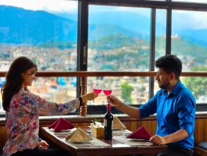 un uomo e una donna seduti a un tavolo con bicchieri da vino di Drishya Hotel a Kathmandu