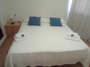 a white bed with two blue pillows on it at Apartamento Illa Blanca in Es Pujols
