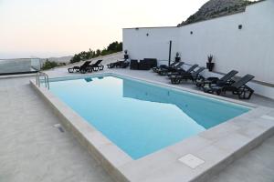 a large swimming pool with chairs and a building at Villa Panorama - Private heated pool and jacuzzi with ocean view in Ivanica