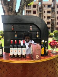 Una mujer parada detrás de una mesa con botellas de vino. en Lotties, en Kampala