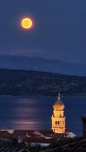 een volle maan die 's nachts boven een gebouw opkomt bij Studio Apartments Maslinik in Krk