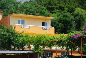 une maison jaune avec un balcon blanc et des arbres dans l'établissement Villa Elvira, à Gradac