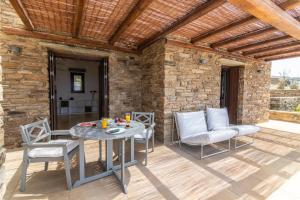 a patio with a table and chairs and a stone wall at Dolce Villa Tinos - Kardiani - Stone & Sunset Views in Kardhianí