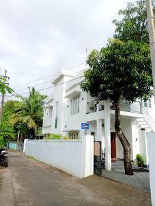 a white house with a tree in front of it at Rohini Homestay & Serviced Villa-Explore Alleppy in Alleppey