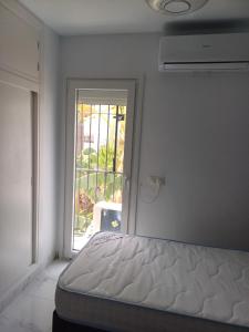 a white bedroom with a bed and a window at Beautiful Beachfront Newly Renovated 2 Bedroom Apartment with Swimming Pool and Garden in San Luis de Sabinillas
