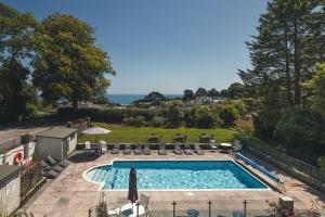 a swimming pool with chaises and chairs and the ocean at Stoke Lodge Hotel in Stoke Fleming