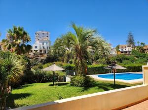 a pool with palm trees and umbrellas in a yard at Jardines de Burriana in Nerja