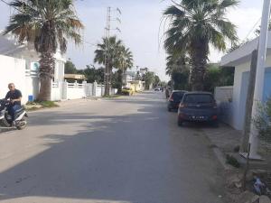 une rue avec des palmiers et un homme sur un scooter dans l'établissement Appartement deux chambres-calme proche plage, à Ḩammām al Ghazzāz 7 autres photos