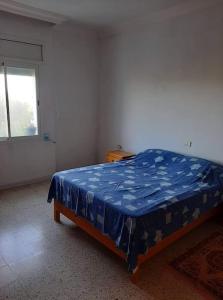 une chambre avec un lit avec une couette bleue et une fenêtre dans l'établissement Appartement deux chambres-calme proche plage, à Ḩammām al Ghazzāz