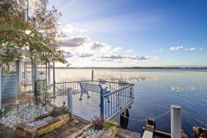 a house with a bench on a dock in the water at Luxury Waterfront Holiday Home in Toukley