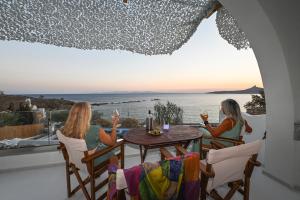 two women sitting at a table on a balcony with a view of the ocean at VETUS PORTUM SUITES TINOs in Tinos Town