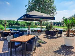 a patio with tables and chairs and an umbrella at 6-p Wellnesshuisje met sauna/hottub bij Nijmegen in Ewijk