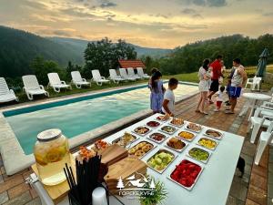 a group of people standing around a table with food next to a pool at Gorske Kuće in Koštunići