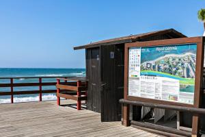 Un paseo marítimo con un banco y un cartel en la playa. en @SeaFront, en Sitio de Calahonda