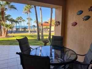 a glass table and chairs on a patio with palm trees at Sandy Beach Princesa D107 Ocean Front Resort in Puerto Peñasco
