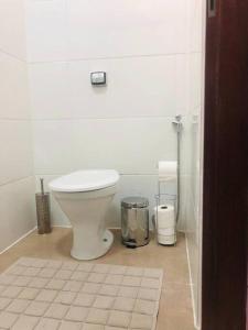 a white bathroom with a toilet and a trash can at Suíte confortável no centro in Delfinópolis