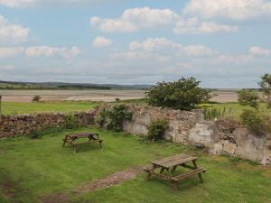 two picnic tables in a field next to a stone wall at Budle Bay Cottage in Bamburgh