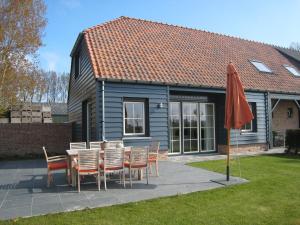 a table and chairs and an umbrella in front of a house at Rural holiday home with outdoor pool & sauna in Zuidzande