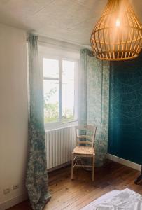 Cette chambre comprend une chaise, une fenêtre et un lustre. dans l'établissement Maison 2 chambres- grand jardin-WIFI - au cœur du village AUBETERRE -visites- conciergerie J&N, à Aubeterre-sur-Dronne