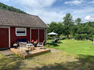 a red house with a deck and chairs in a yard at Riverside Bliss - Cozy Cabin near Tvedestrand with WiFi and Deck in Vegårshei