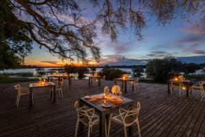a group of tables and chairs on a deck with a sunset at Chundu Island in Victoria Falls
